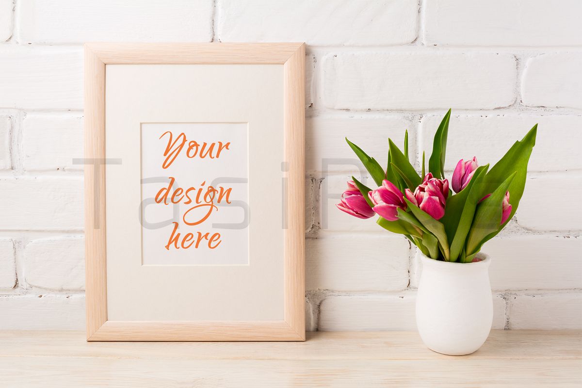 Wooden frame mockup with magenta pink tulips bouquet in white flower pot near painted brick wall.