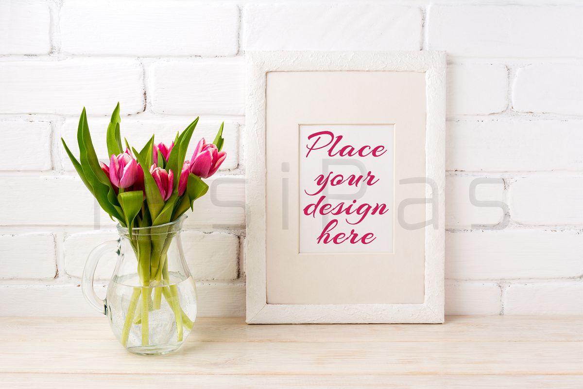 White frame mockup with magenta pink tulips bouquet in glass jug near white painted brick wall. example image 1