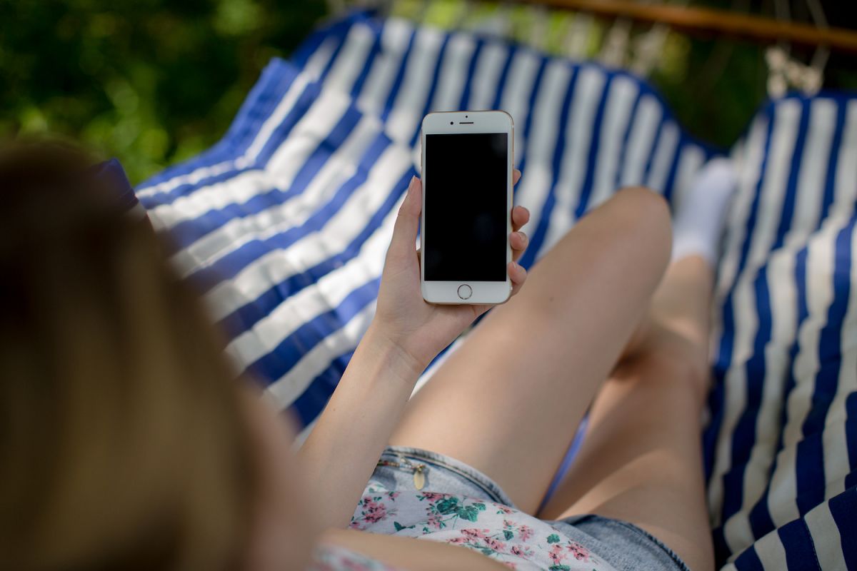 Young lady on hammock holding smartphone with blank screen example image 1