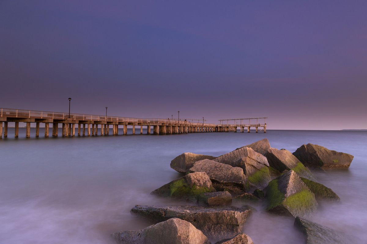 View on the pier in ocean from the rocky beach at sunset wit example image 1