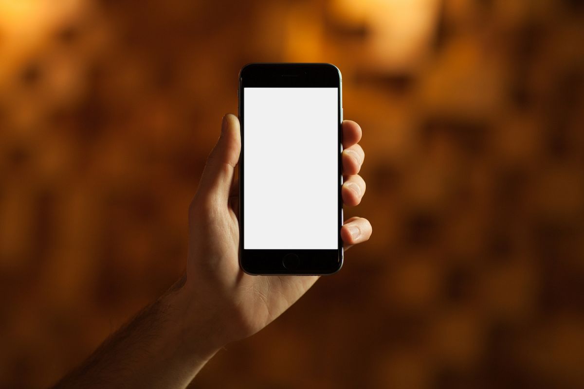 Male hand holding smartphone with blank screen on wood background example image 1